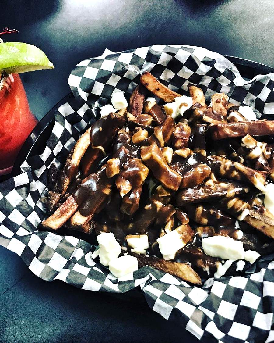 Poutine: home-cut fries smothered in dark gravy and cheese curds, served in a black-and-white checkered basket