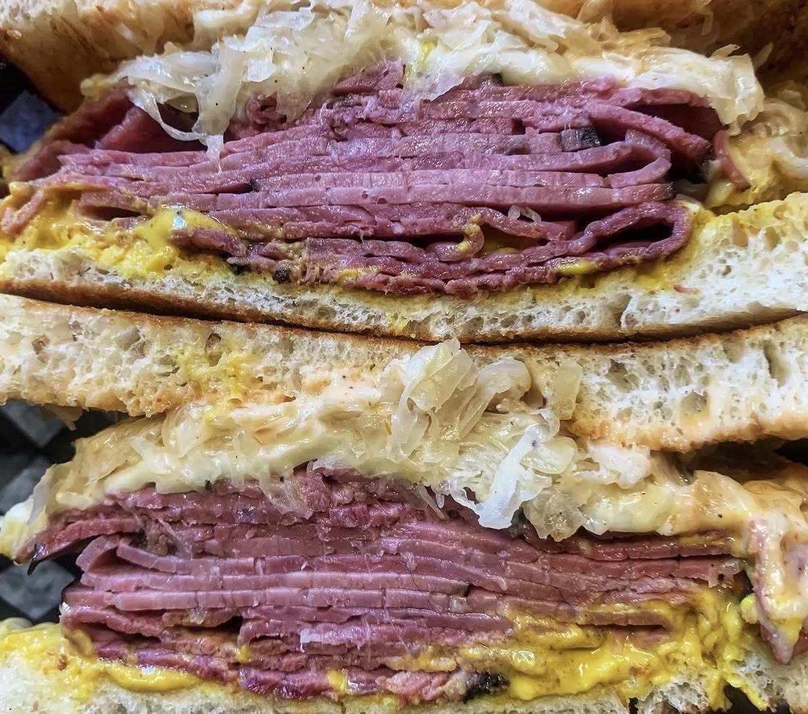 A stacked sandwich piled high with thin-sliced smoked meat, melted Swiss and sauerkraut on grilled bread