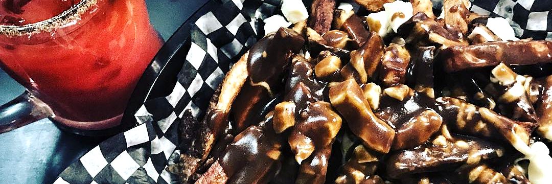 Regular poutine: home-cut fries with cheese curds and dark gravy in a black-and-white checkered basket